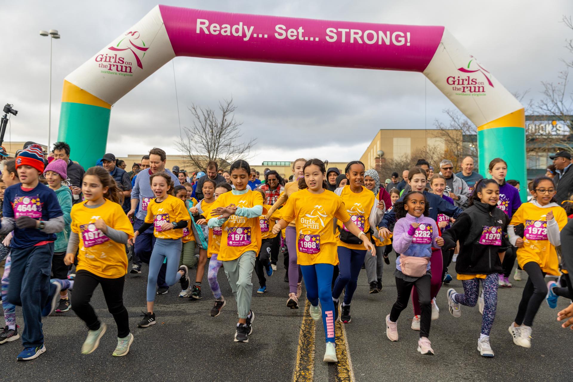 Girls on the Run participants and Buddy Runners running across the 5K start line.