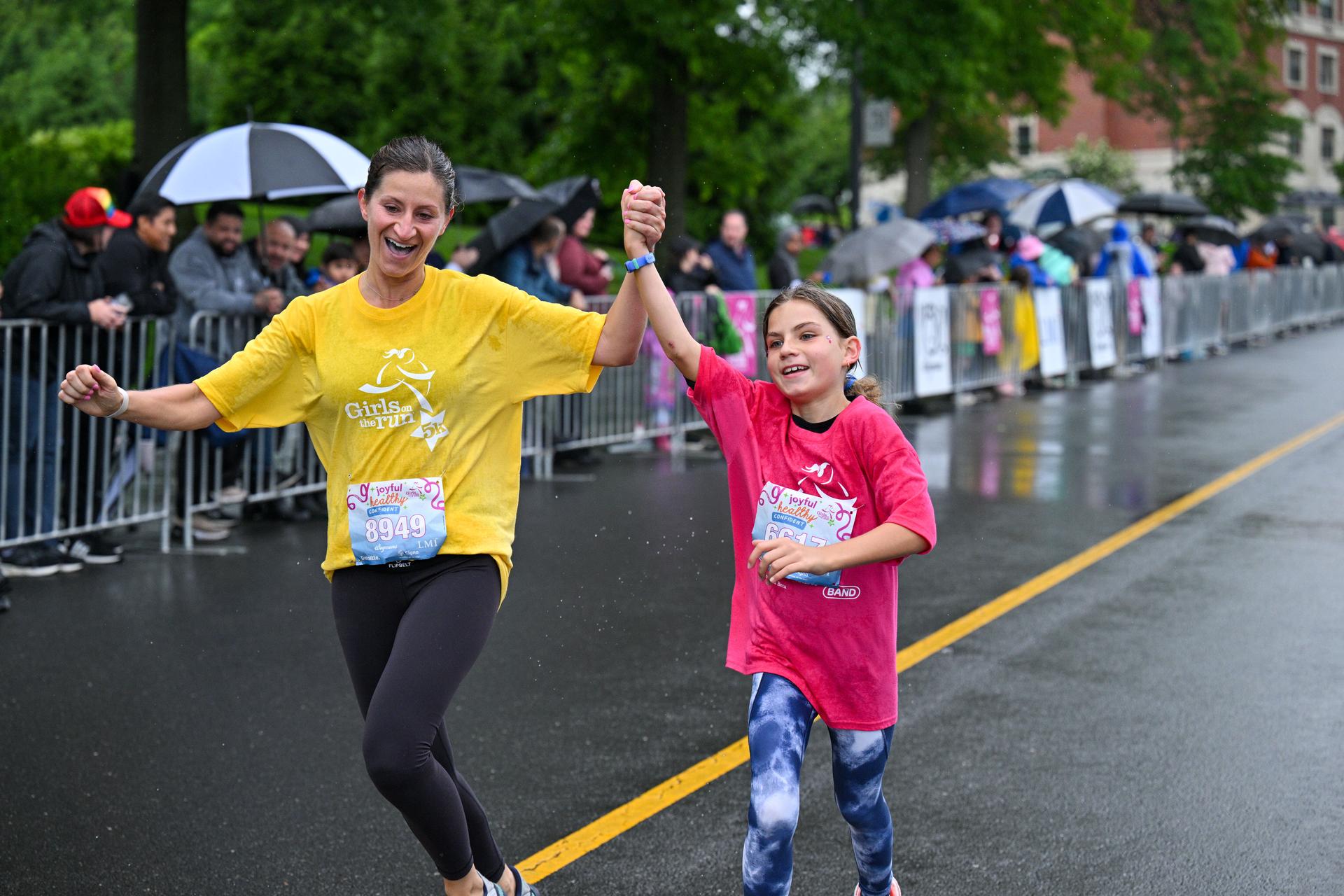 An adult and child running with their hands interlocked and raised in the air.