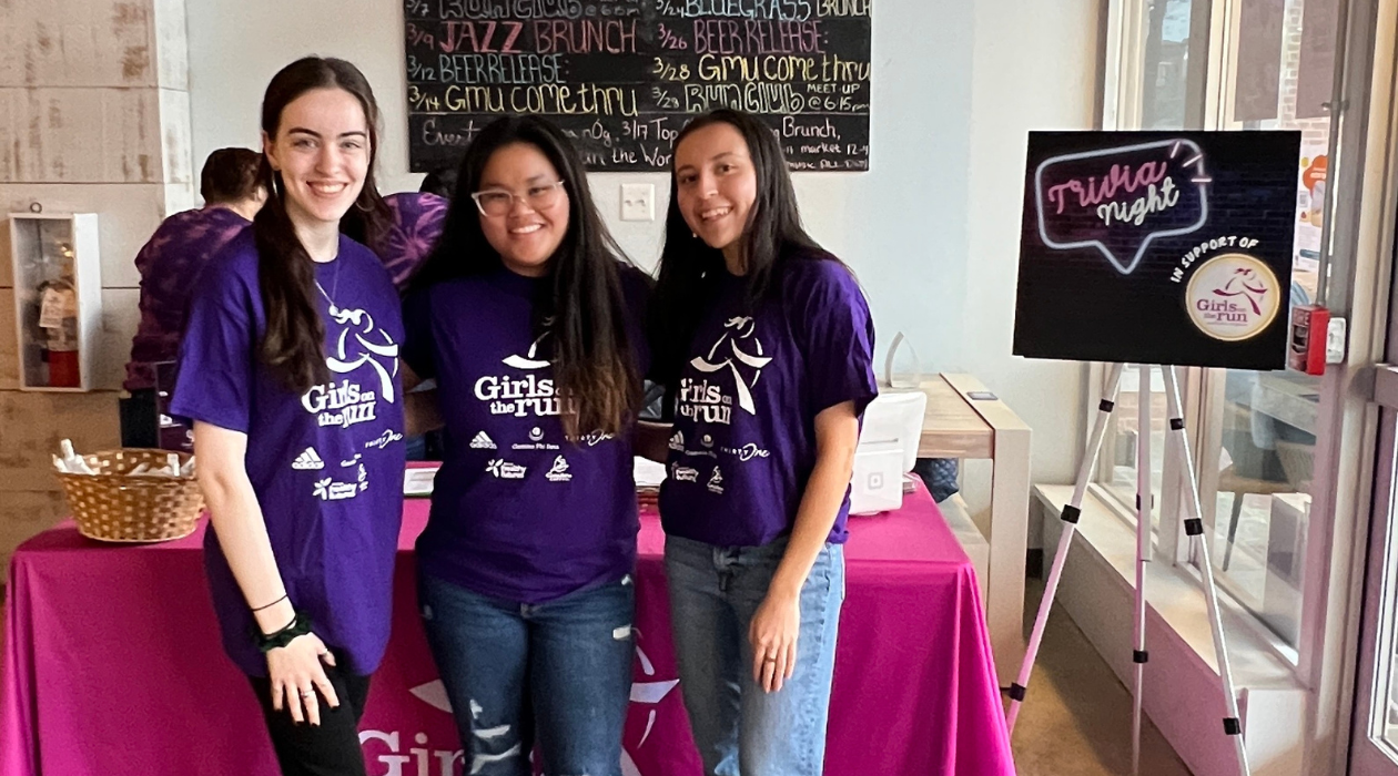 Three girls smiling as they pose for a picture wearing purple Girls on the Run t-shirts.