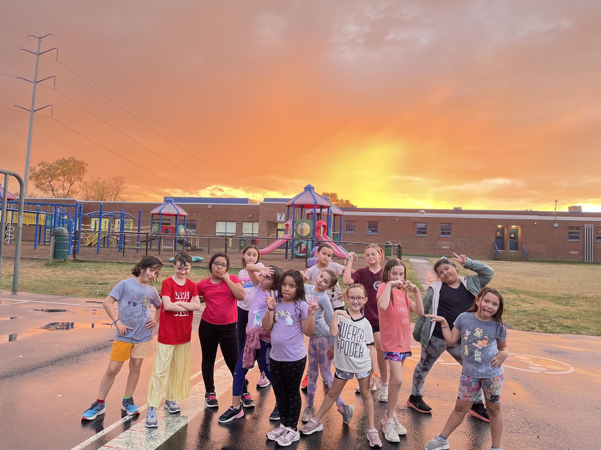 Girls on the Run team posing for a photo in front of a bright orange and yellow sunset.