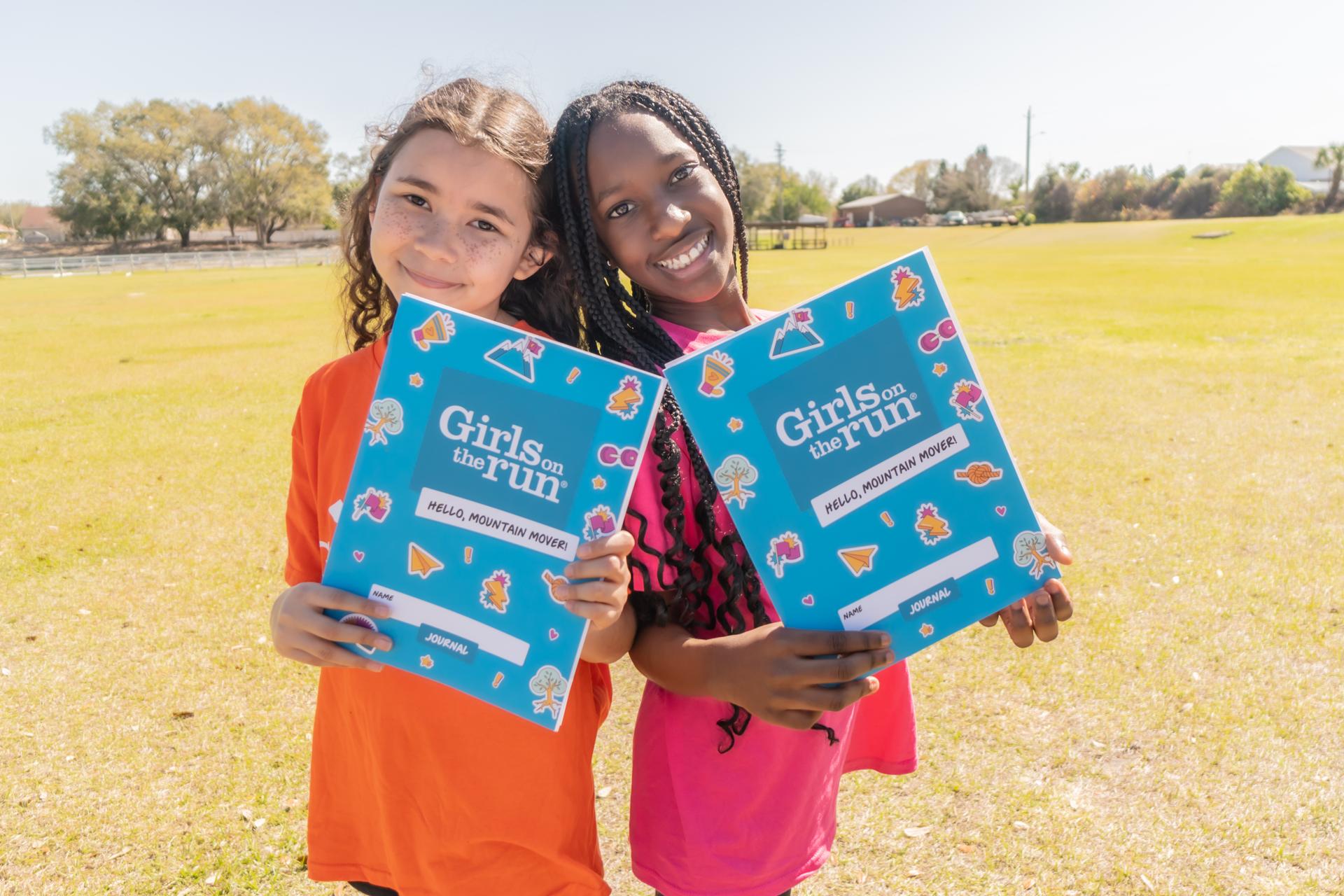 Two Girls on the Run participants holding up journals and smiling.