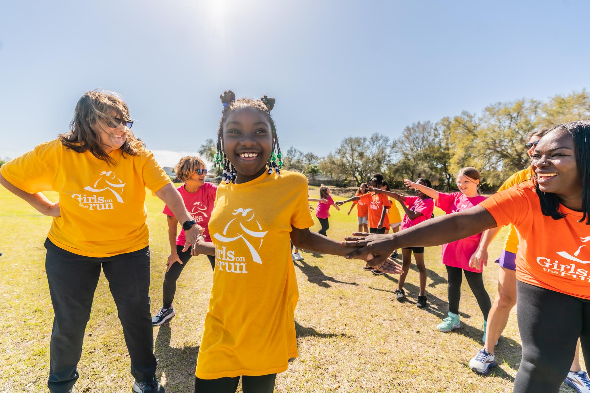 A Girls on the Run participant smiling and high fiving her coaches with the rest of her team smiling and cheering behind her.